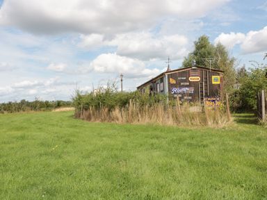 A green grassy field with a fenced area containing a wooden shed with vintage signs in a rural setting