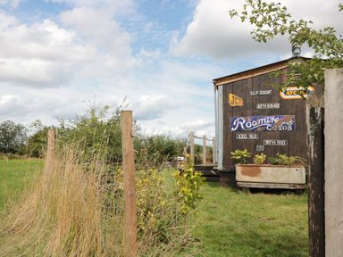 A rustic wooden shed with vintage signs and a planter box next to a grassy field with tall dry grass at Crows Cabin in Gloucester