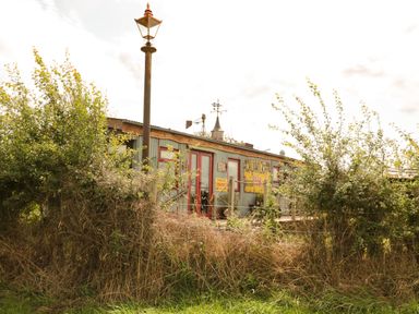 An outdoor scene with a lamppost shrubs and a weathered building with signs at Crows Cabin in Gloucester