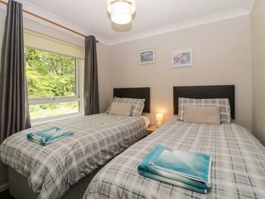A bedroom with two single beds with checkered bedding and folded towels near a window at Tranquillity Rosecraddoc Lodge near Liskeard