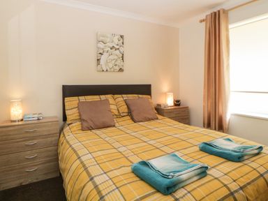 A bedroom with a double bed with yellow plaid bedding and two brown pillows with two bedside tables with lamps at Tranquillity Rosecraddoc Lodge near Liskeard