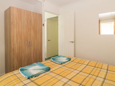A bedroom with a yellow plaid bedspread two folded towels on the bed a wooden wardrobe and a white door at Tranquillity Rosecraddoc Lodge near Liskeard