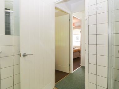 A hallway with open white doors leading to a bedroom and tiled bathroom walls at Tranquillity Rosecraddoc Lodge near Liskeard