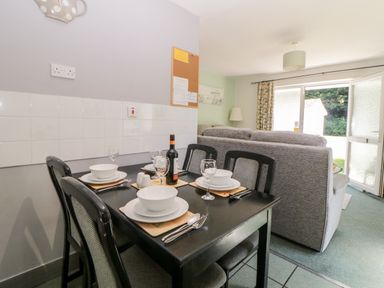 A dining area with a set table and a living room with open door and sofa at Tranquillity Rosecraddoc Lodge near Liskeard