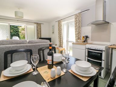 A kitchen dining area with a set table and an oven next to a door and windows with curtains at Tranquillity Rosecraddoc Lodge near Liskeard