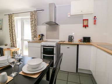 A kitchen with a dining table set with plates and glasses a stove a fridge a kettle and a toaster at Tranquillity Rosecraddoc Lodge near Liskeard