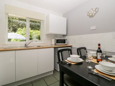 A kitchen with a sink under a window a microwave on the counter and a dining table set with plates bowls glasses and a bottle of wine at Tranquillity Rosecraddoc Lodge near Liskeard
