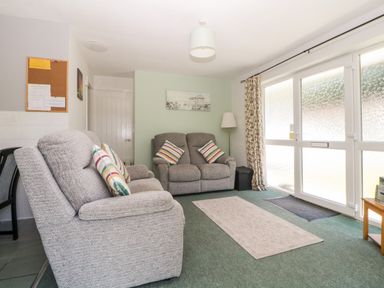 A living room with two grey sofas and striped cushions near large frosted glass doors at Tranquillity Rosecraddoc Lodge near Liskeard