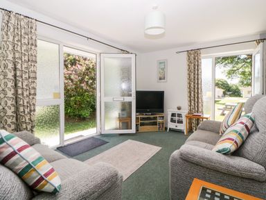 A living room with two sofas a television and open doors to the garden at Tranquillity Rosecraddoc Lodge near Liskeard