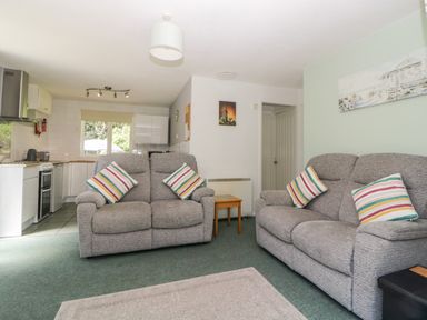 A living room with two grey sofas and striped cushions next to a kitchen at Tranquillity Rosecraddoc Lodge near Liskeard