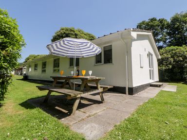 An outdoor picnic table with a striped umbrella and glasses beside a white building at Tranquillity Rosecraddoc Lodge near Liskeard