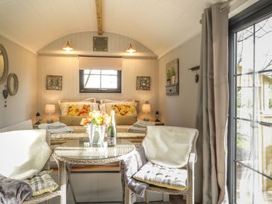 A bedroom with a bed pillows and lamps with two chairs and a table with flowers and champagne in High Rigg Shepherds Delight in Brampton Cumbria