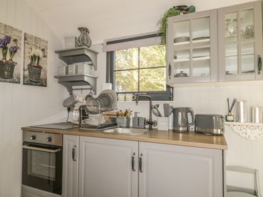 A kitchen with grey cabinets a countertop with appliances and dish rack under a window at High Rigg Shepherd's Delight in Brampton Cumbria