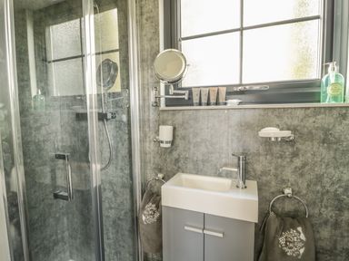 A bathroom with a shower enclosure a small sink cabinet and towels hanging on rings at High Rigg Shepherds Delight in Brampton Cumbria