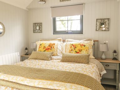 A bedroom with a bed with yellow floral bedding under a window with two bedside tables and lamps at High Rigg Shepherd's Delight in Brampton Cumbria