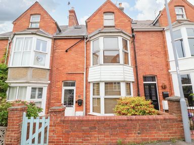 A row of brick houses with bay windows and a small front garden behind a low brick wall at Brewers House in Weymouth