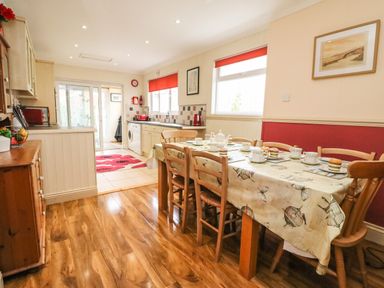 A kitchen and dining area with wooden chairs around a table covered with a patterned tablecloth and kitchen appliances on counters at Brewers House in Weymouth