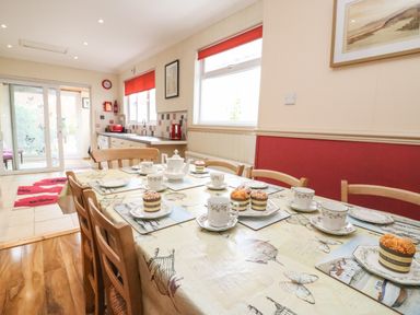 A dining area with a table set for tea and cupcakes next to a kitchen with red accents at Brewers House in Weymouth