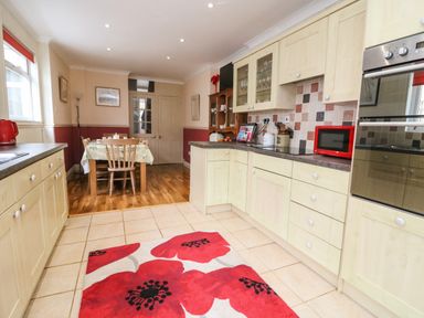 A kitchen with wooden cabinets tiled floor red microwave and dining area at Brewers House in Weymouth