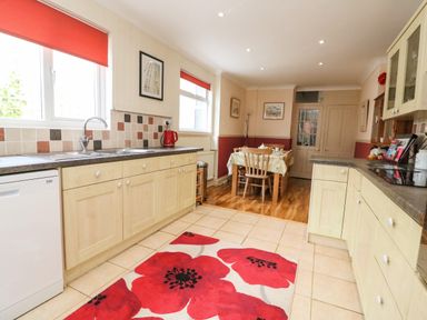 A kitchen with wooden cabinets a dining table with chairs and red window blinds at Brewers House in Weymouth