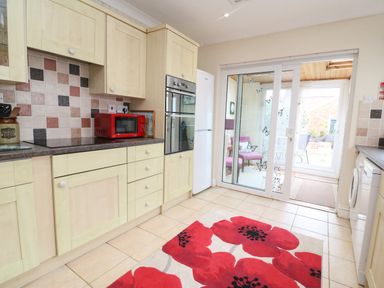 A kitchen with light wood cabinets red microwave and double oven next to glass sliding doors leading to a seating area at Brewers House in Weymouth