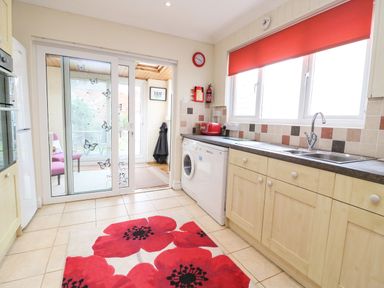 A kitchen with light wooden cabinets a red toaster and a red clock a washing machine under the counter and sliding glass doors with butterfly decals at Brewers House in Weymouth