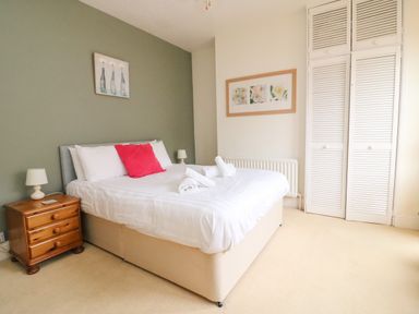 A bedroom with a double bed with white bedding and red pillow a wooden nightstand a lamp and built in white wardrobes at Brewers House in Weymouth
