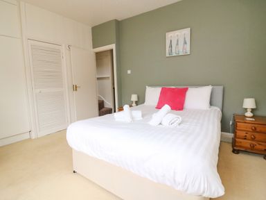 A bedroom with a bed with white bedding and a pink pillow bedside tables with lamps and a door at Brewers House in Weymouth