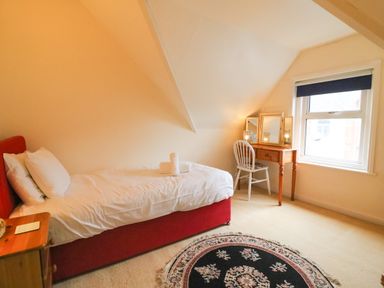 A bedroom with a single bed beside a wooden nightstand and a dressing table with a chair near a window at Brewers House Weymouth