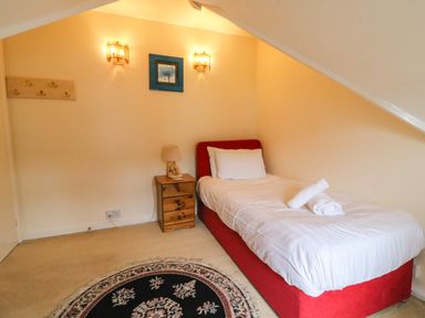 A bedroom with a single bed with white bedding a wooden nightstand with a lamp a circular patterned rug on the floor and slanted ceiling at Brewers House Weymouth