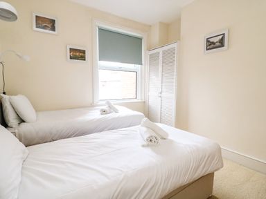 A bedroom with two single beds with white linens and rolled towels near a window with a blue blind at Brewers House in Weymouth