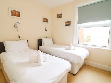 A bedroom with two single beds white bedding and towels on each bed and wall lamps above at Brewers House in Weymouth
