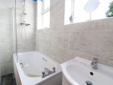 A bathroom with a bathtub shower combo a sink and two windows with decorative items on the sill at Brewers House in Weymouth