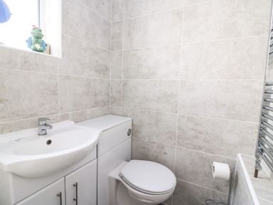 A bathroom with a sink, toilet, tiled walls, and a window with a frog figurine at Brewers House in Weymouth