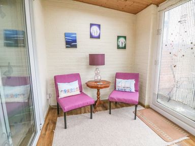 Two purple chairs with cushions beside a wooden side table with a lamp in a room with white brick walls and large windows at Brewers House in Weymouth