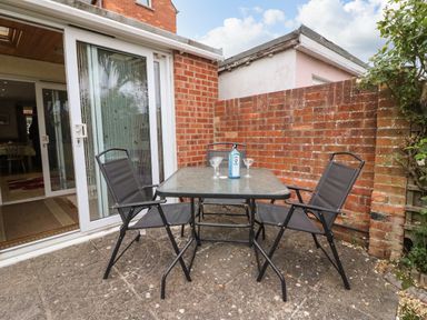 A small patio with a glass table and three black chairs next to a brick wall and sliding glass doors at Brewers House in Weymouth