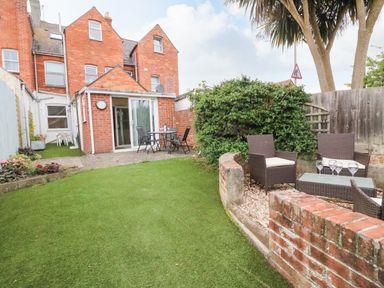 A backyard garden with artificial grass a patio table with chairs and a seating area with wicker chairs and a glass table at Brewers House in Weymouth