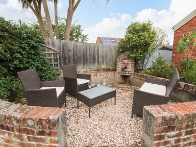 An outdoor seating area with three chairs and a table with glasses on a gravel surface surrounded by brick walls and plants at Brewers House in Weymouth