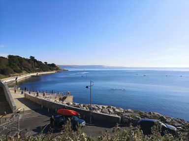 A coastal walkway with people exercising by the water and kayaks on a car at Brewers House in Weymouth