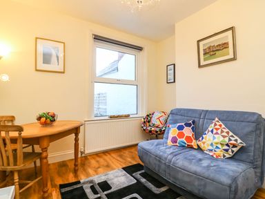 A small living room with a wooden table and chairs a window a blue sofa with colorful cushions a patterned chair and pictures on the walls at Brewers House in Weymouth