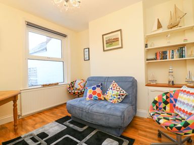 A living room with a blue sofa and patterned chairs by a window and bookshelf at Brewers House in Weymouth