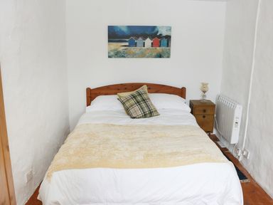 A bedroom with a wooden bed a plaid pillow a side table with a lamp and a painting on the wall at An Teach Ban in Rossaveel County Galway