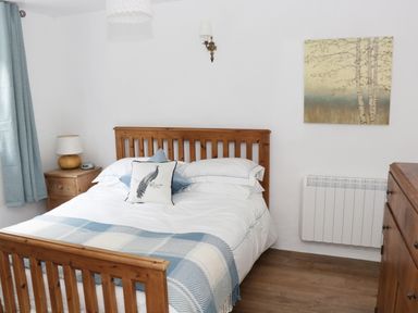 A bedroom with a wooden bed frame a bedside table with a lamp curtains and a painting on the wall at An Teach Ban in Rossaveel County Galway