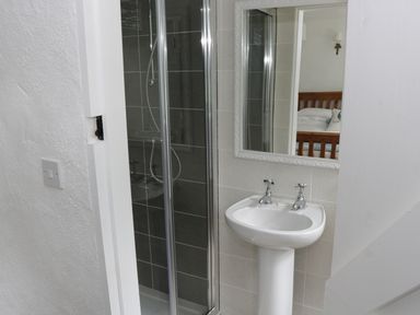 A bathroom with a shower cabin sink and mirror reflecting a bedroom at An Teach Ban in Rossaveel County Galway