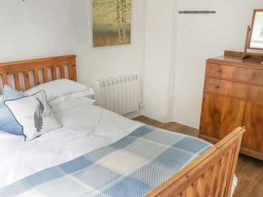 A bedroom with a wooden bed frame blue and white bedding a wooden dresser and a painting on the wall at An Teach Ban in Rossaveel County Galway