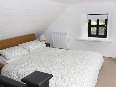 A bedroom with a bed with patterned bedding a lamp on a side table a wall heater and a window at An Teach Ban in Rossaveel County Galway