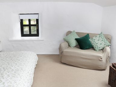 A small room with a beige sofa with green pillows a bed with patterned bedspread and a small window at An Teach Ban in Rossaveel County Galway