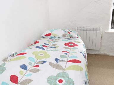 A single bed with floral patterned bedding in a white room with a radiator at An Teach Ban in Rossaveel County Galway