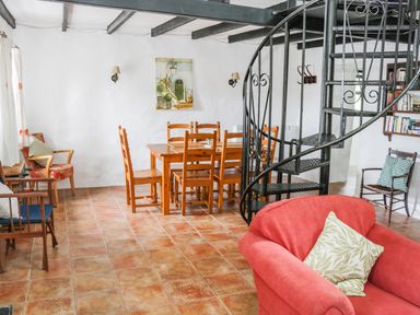 A dining area with a wooden table and chairs near a black spiral staircase and seating at An Teach Ban in Rossaveel County Galway