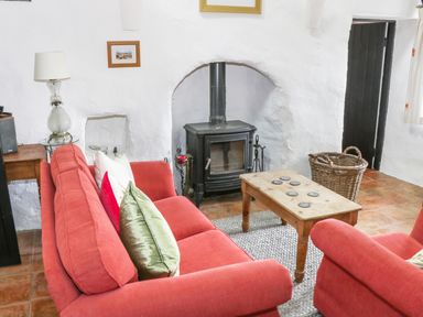 A living room with red sofas a wooden coffee table a black wood stove and a wicker basket at An Teach Ban in Rossaveel County Galway